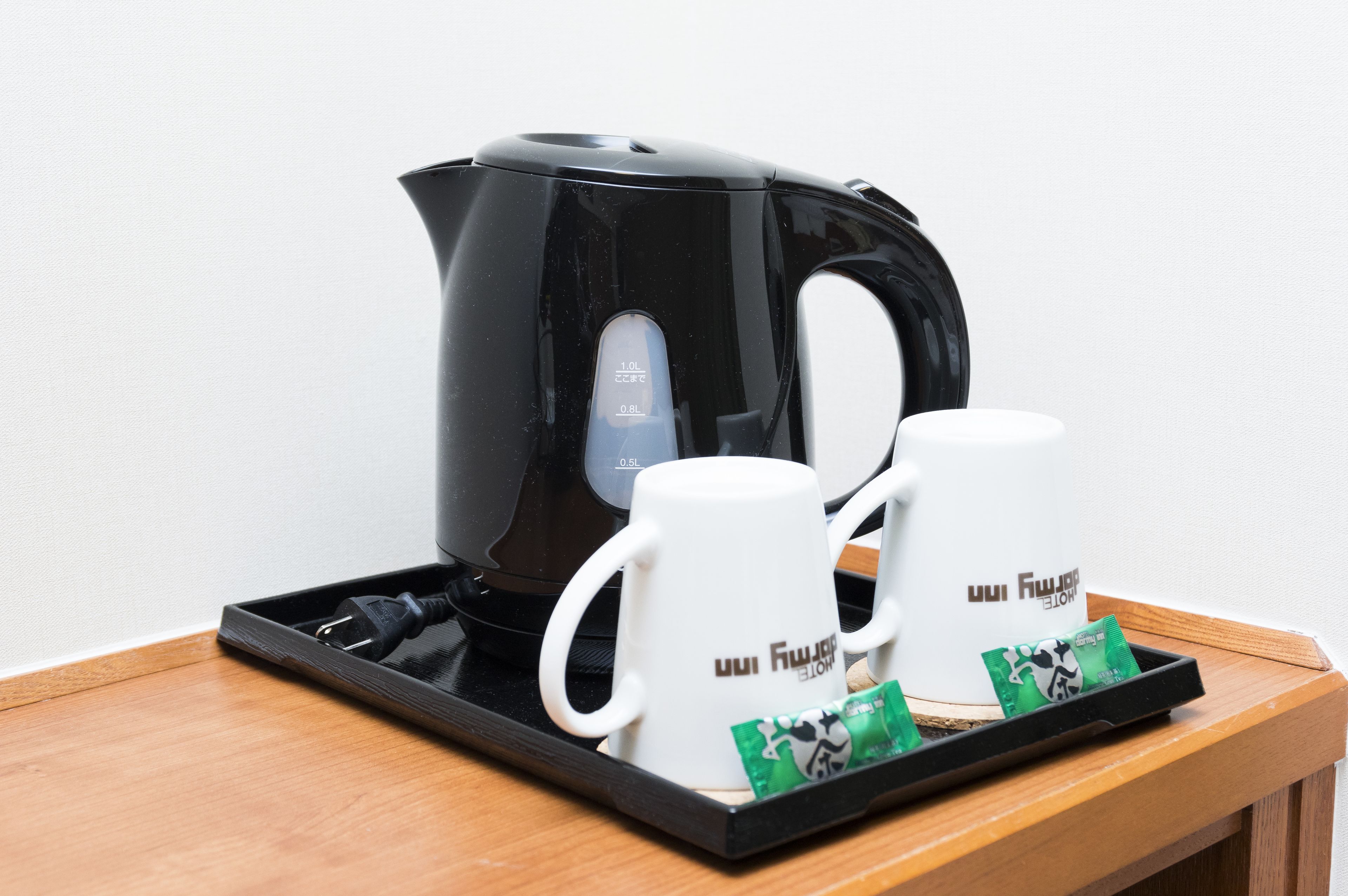 A black electric kettle on a tray with two white mugs and green tea packets.