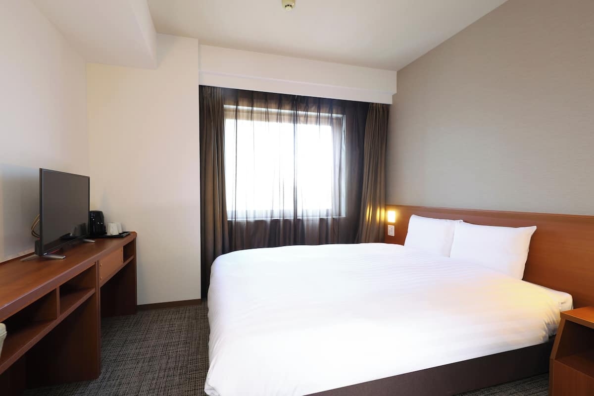 A hotel room with a large bed, a desk with a computer, and a window with curtains.