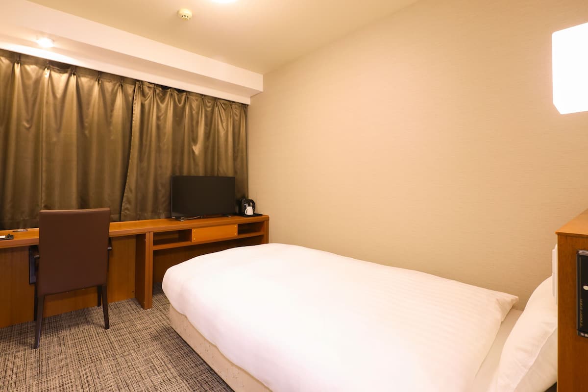 A hotel room with a bed, a desk, a chair, a television, and curtains.