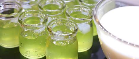 A tray with multiple small glass containers filled with a green liquid, likely a beverage, and a larger bowl with a white substance, possibly a food item, on a reflective surface.