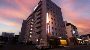 Un hotel de varios pisos con un letrero vertical llamativo, varios balcones y un estacionamiento al frente.