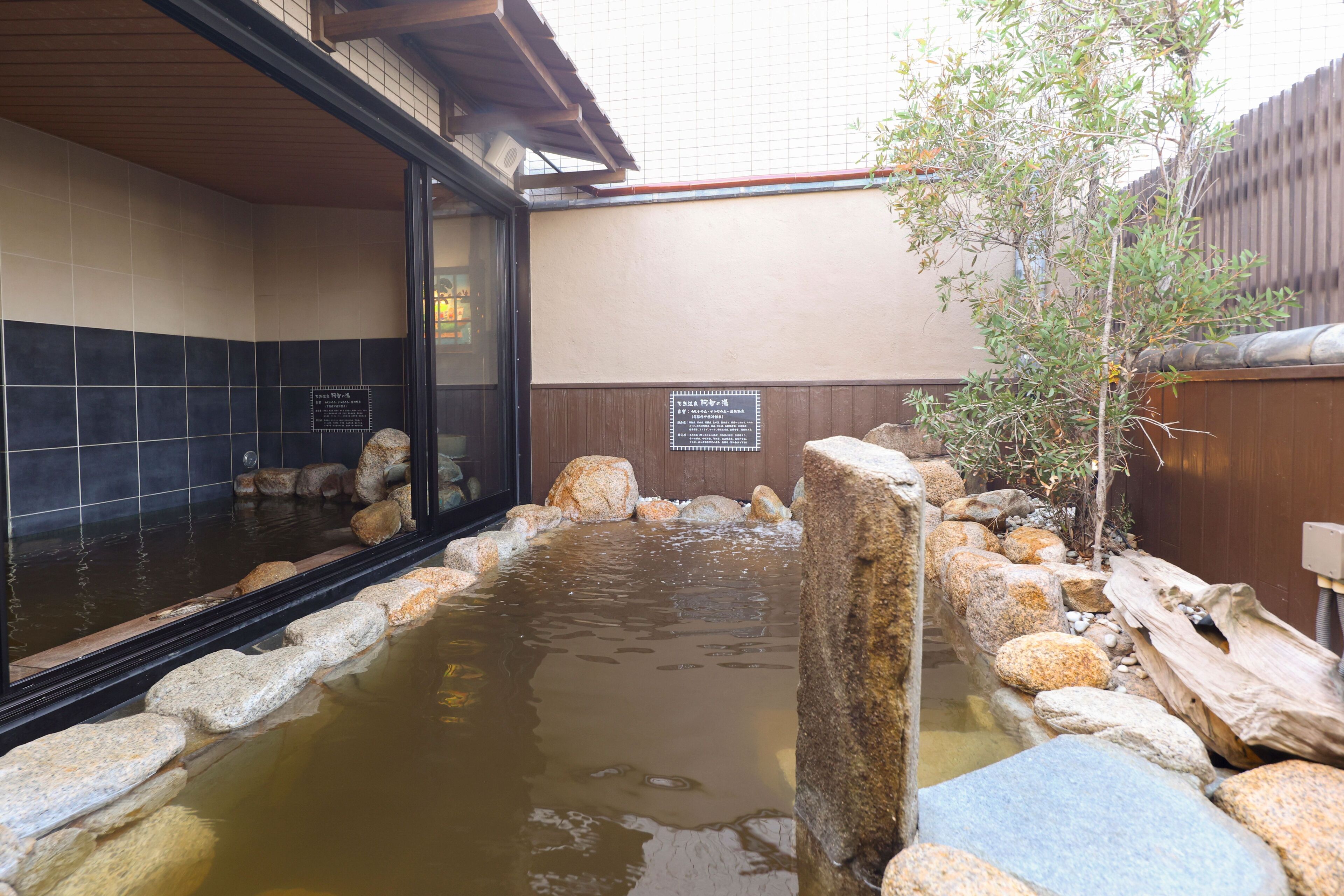 A traditional Japanese onsen with a stone bath surrounded by rocks and a wooden fence.