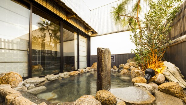 Un onsen japonés tradicional con una bañera de piedra rodeada de rocas y una valla de madera.