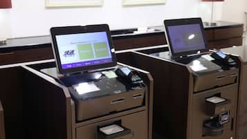Two self-service kiosks with digital screens, a desk, and framed artwork on the wall.