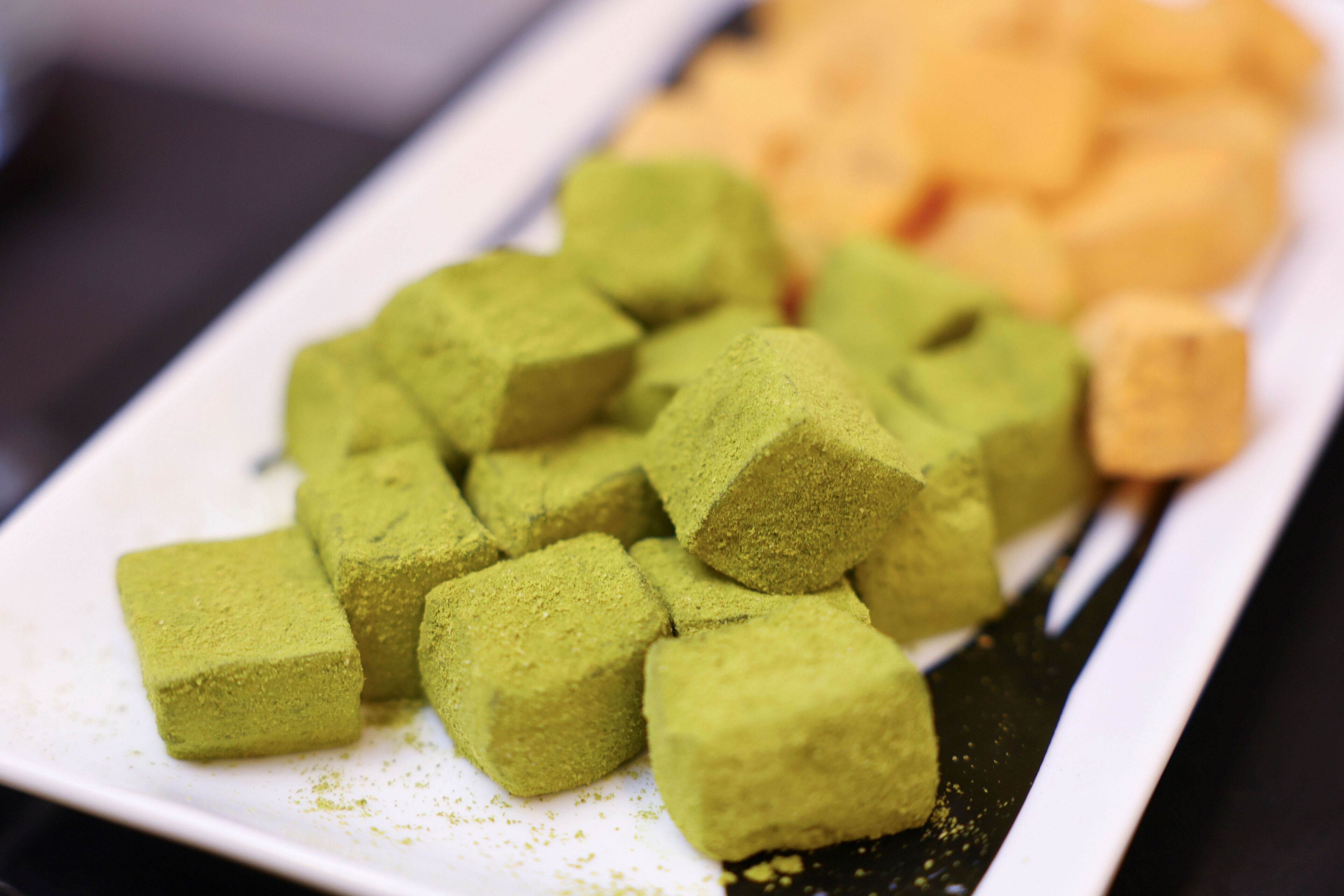 A plate of matcha cubes and a small piece of tofu on a white plate.