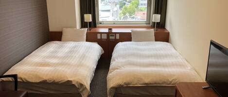 A hotel room with two beds, a desk, a chair, a TV, and a window with a city view.