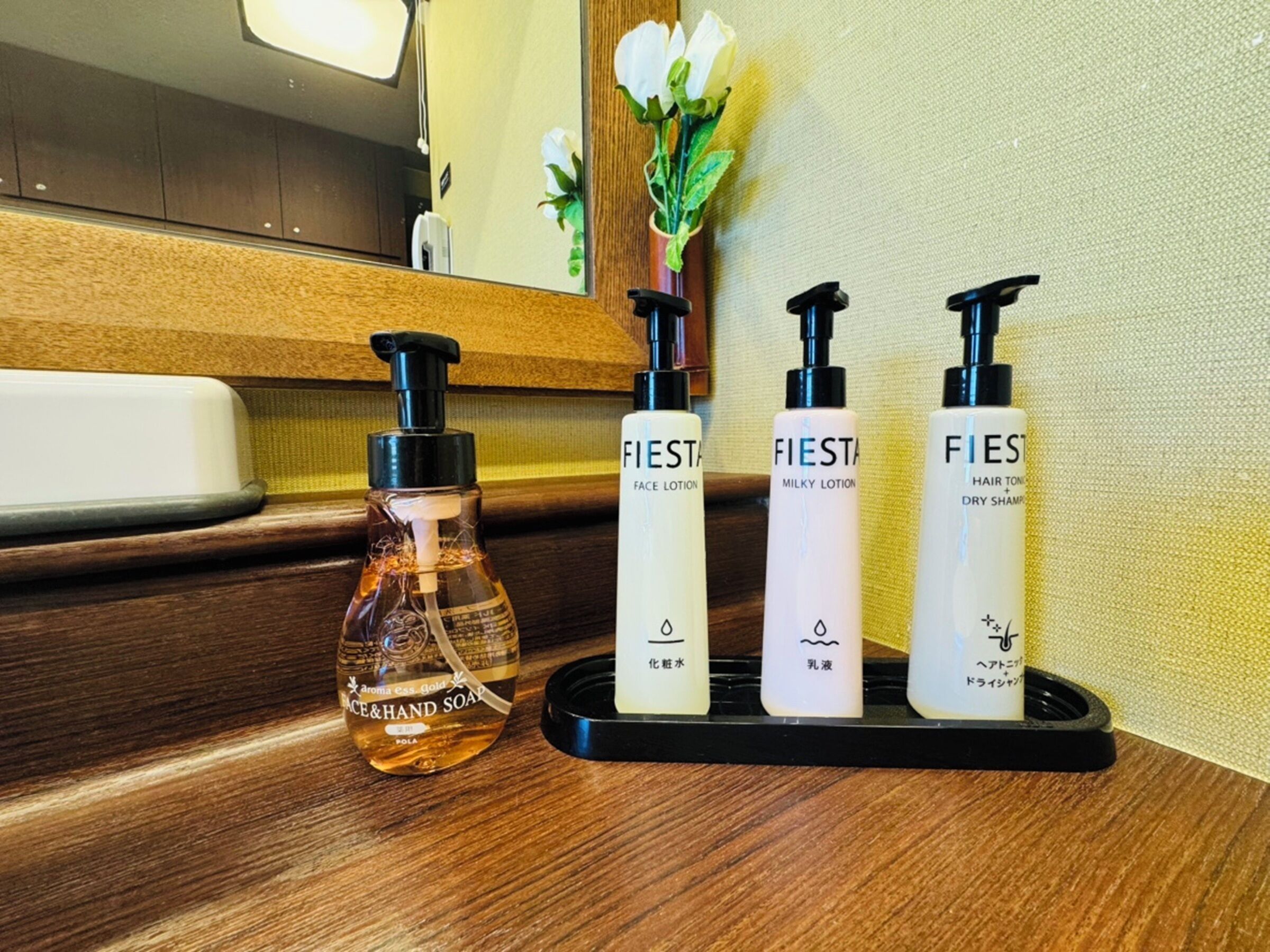 A bathroom vanity with a mirror, a bottle of face and hand soap, and three bottles of FIESTA hair and dry shampoo.