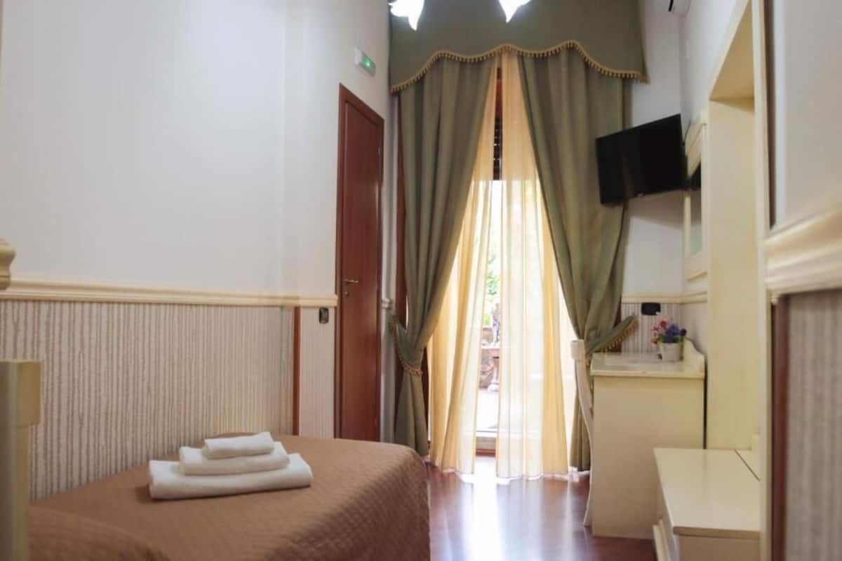 A hotel room with a bed, a desk, a television, and a window with curtains.