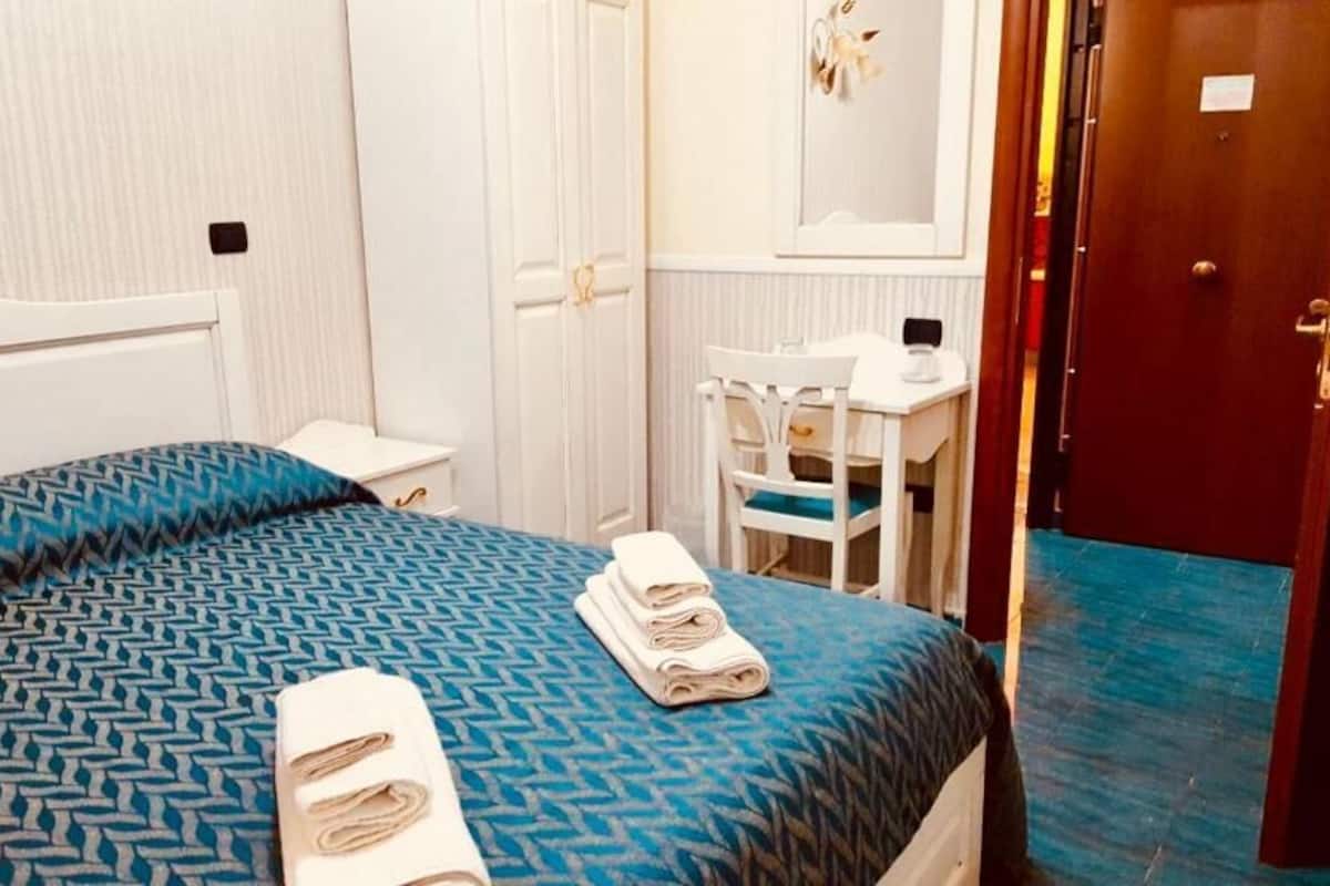 A hotel room with a bed, a desk, a chair, and a wardrobe.