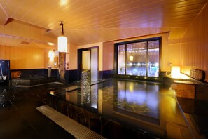A modern spa with a large hot tub, wooden paneling, and a view of a traditional Japanese building. - Dormy Inn Sendai Ekimae (Sendai)