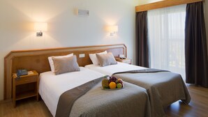 Ein Hotelzimmer mit zwei Betten, einem Nachttisch mit Telefon und einer Obstschale auf den Betten.