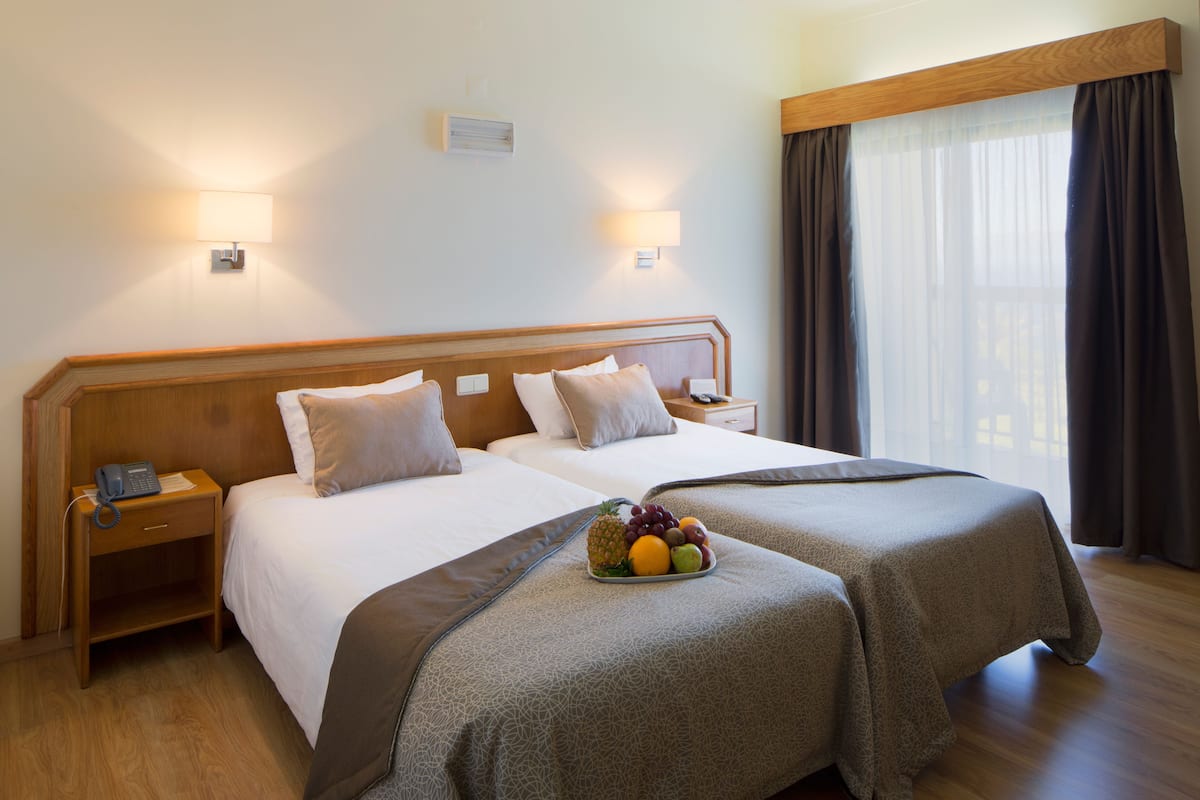 A hotel room with two beds, a bedside table with a phone, and a fruit bowl on the beds.