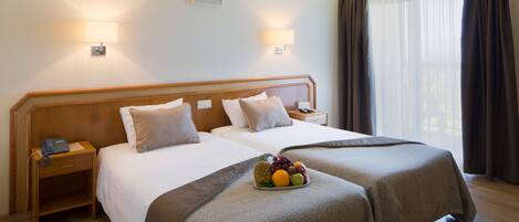 A hotel room with two beds, a bedside table with a phone, and a fruit bowl on the beds.