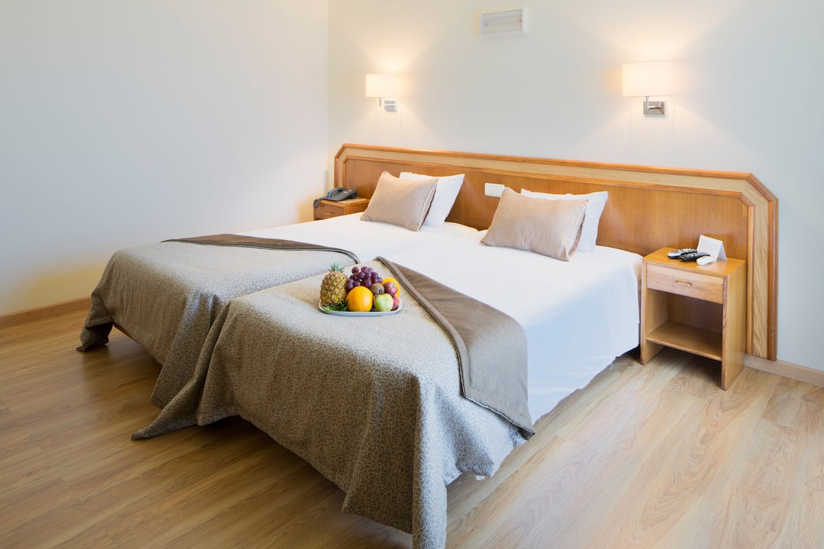 A hotel room with a large bed, two bedside tables, and a fruit basket on the bed.