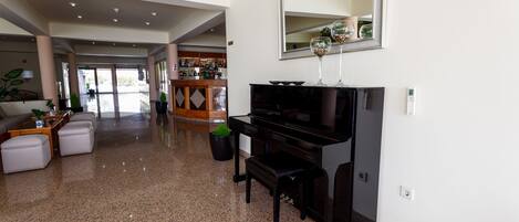 A spacious living room with a black piano, a large mirror, and a bar area in the background.