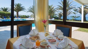 Ein Esstisch, gedeckt für das Frühstück, mit Blick auf einen Pool und Palmen.