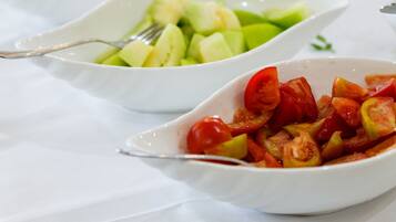 Et bord med forskellige retter, heriblandt en frugtsalat, en tomatsalat og et glas appelsinjuice.