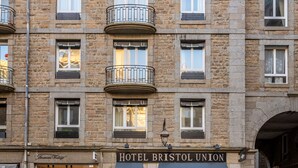 Un hotel de varios pisos con fachada de piedra, balcones y un espacio comercial en la planta baja.
