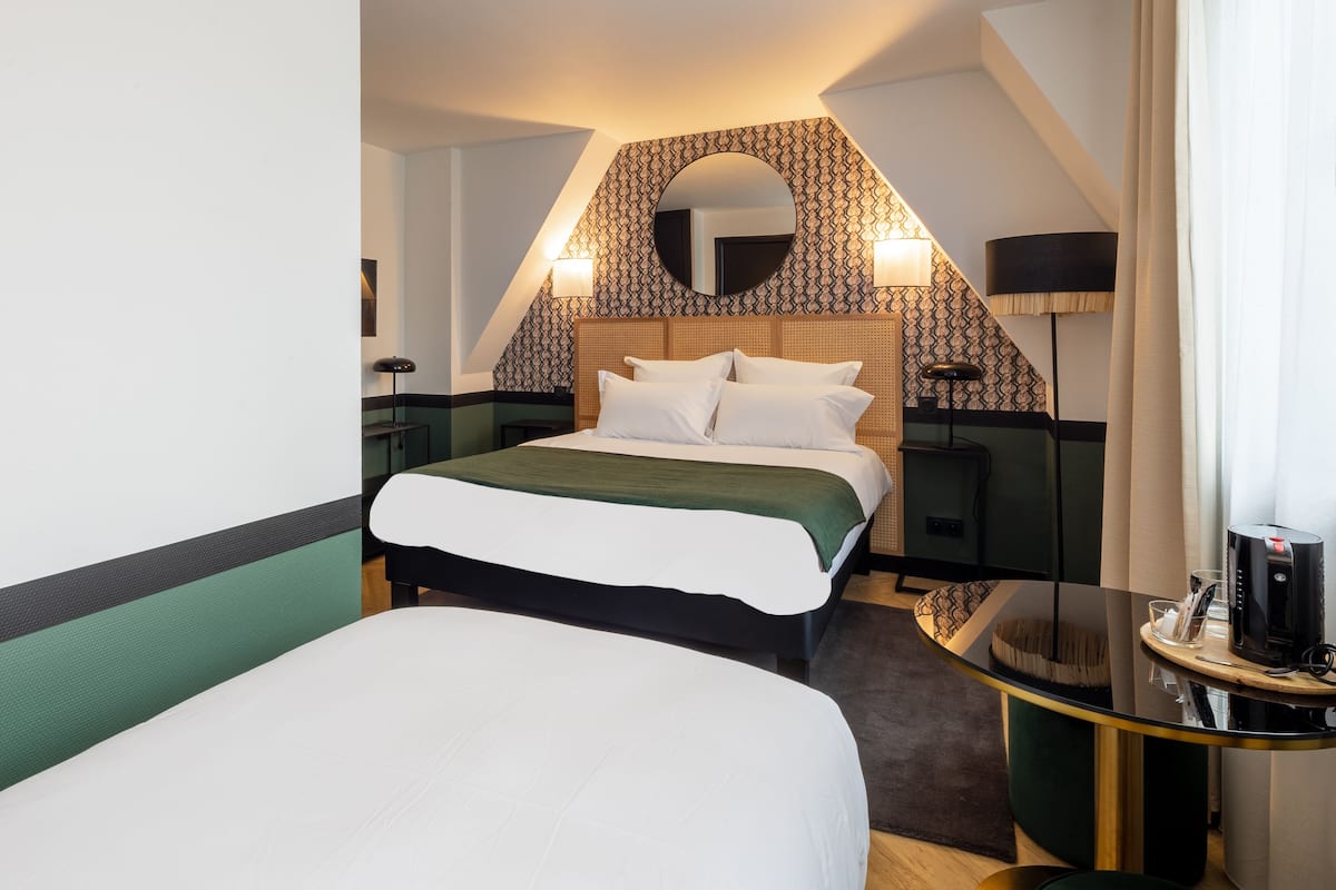 A hotel room with a bed, a round mirror, a lamp, and a small table with a coffee maker.