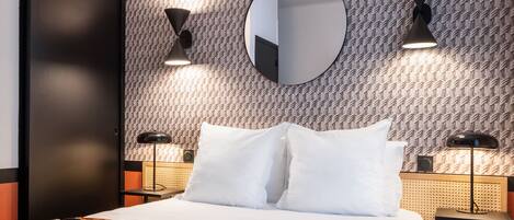 A hotel room with a bed, two bedside tables, a round mirror, and wall-mounted lamps.