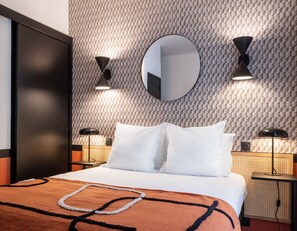 Een hotelkamer met een bed, twee nachtkastjes, een ronde spiegel en wandlampen.