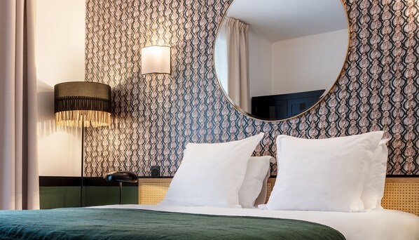 A hotel room with a large bed, a round mirror, a wall-mounted lamp, and patterned wallpaper.