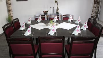 A round dining table with red upholstered chairs, a vase, and decorative paper cones on the tablecloth.