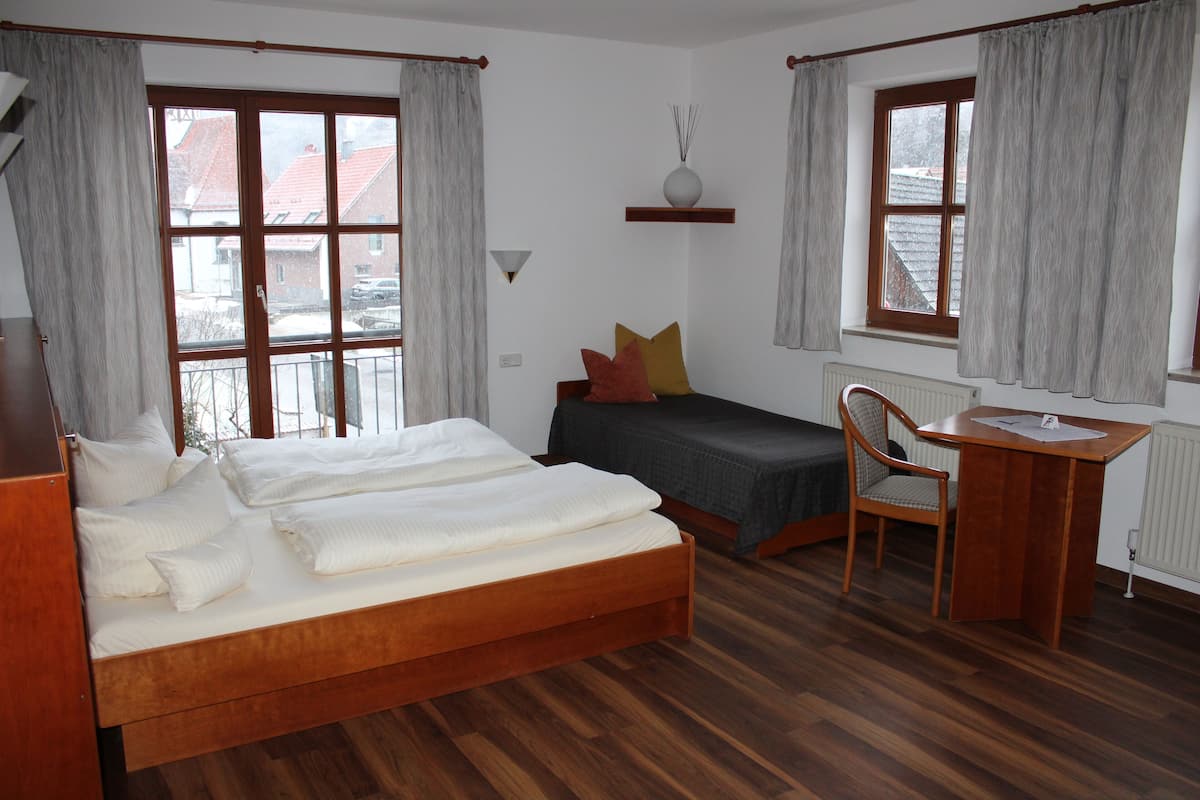 A bedroom with a wooden bed, a desk, and two windows with curtains.