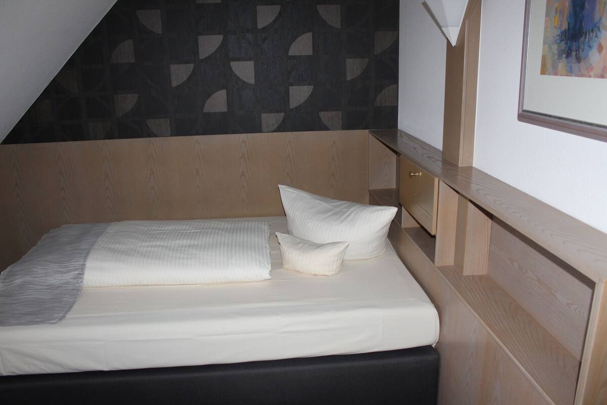 A neatly made bed with a headboard, a bedside table, and a wall with a geometric pattern.