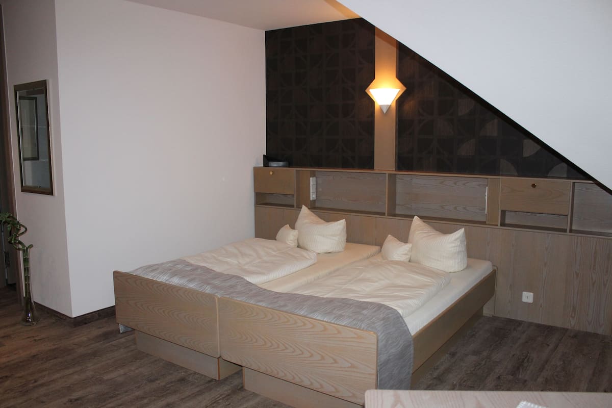 A bedroom with a wooden bed, a nightstand, a wall-mounted light, and a mirror.