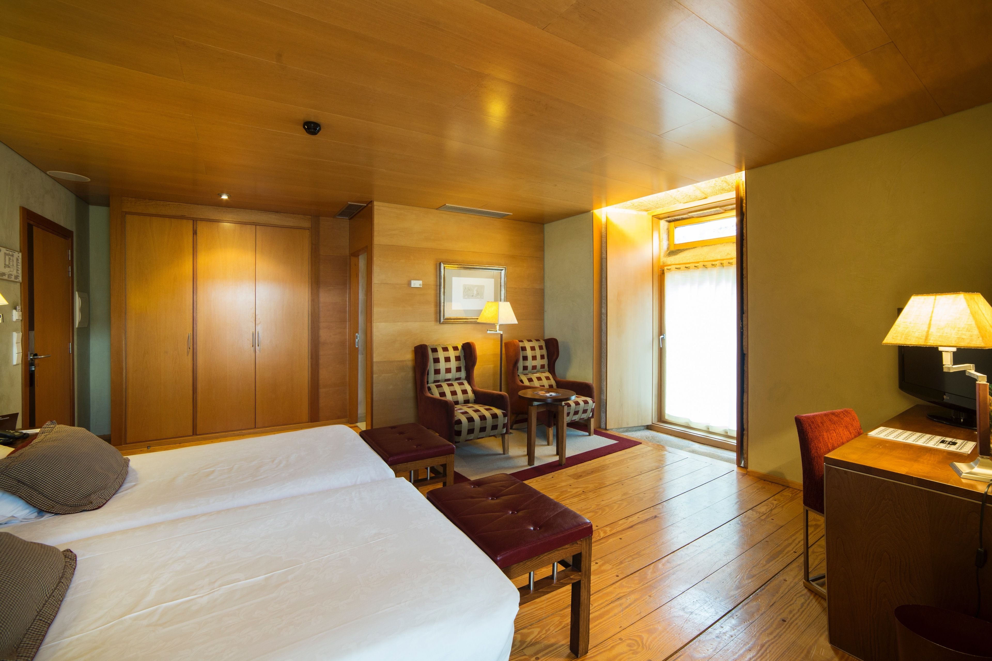 A hotel room with a large bed, two armchairs, a desk with a computer, and a television.