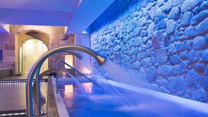 Un espace piscine intérieur moderne, avec un mur en pierre et un élément décoratif aquatique.
