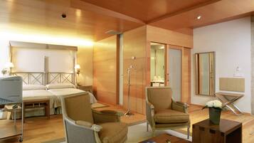 A hotel room with a bed, two armchairs, a coffee table, a mirror, and a bedside table with a lamp.