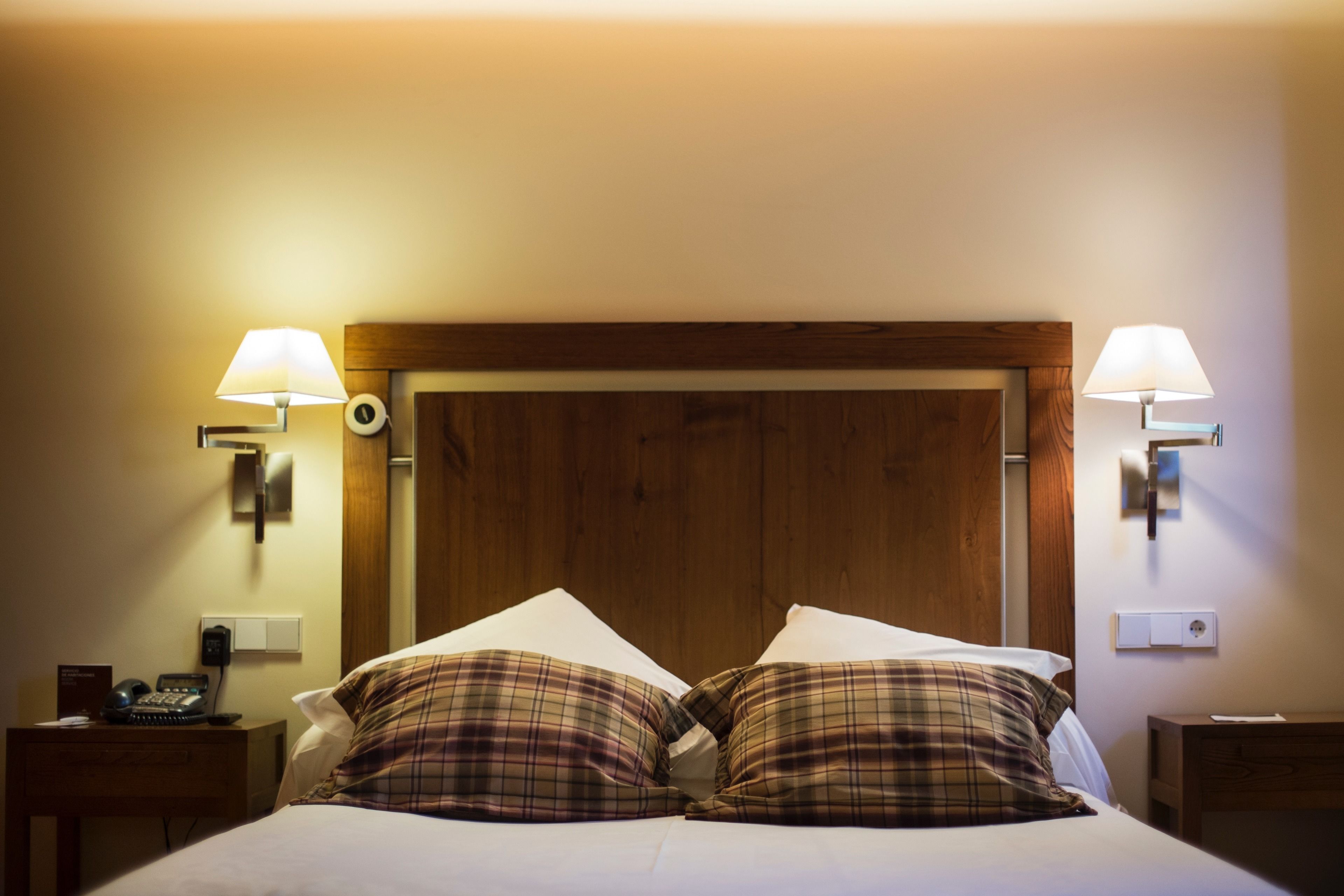 Ett hotellrum med en sänggavel i trä, två sänglampor, en telefon och kuddar med rutmönster.