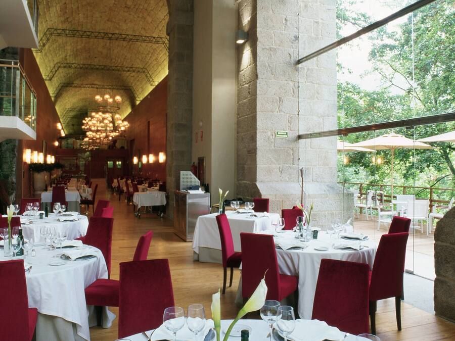 Um restaurante espaçoso com pé-direito alto e paredes de pedra, com várias mesas preparadas para os hóspedes.
