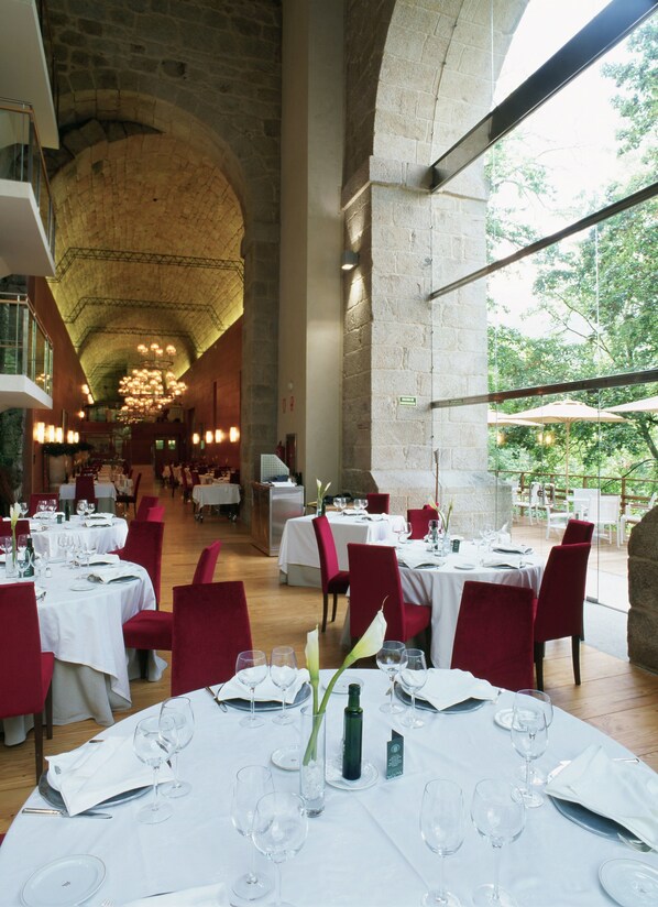Un restaurante espacioso con techos altos y paredes de piedra, con varias mesas dispuestas para los comensales.