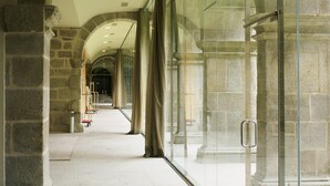 Un couloir aux murs de pierre et aux portes de verre, qui mène à un escalier.