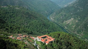Un paisaje montañoso con un río, un pequeño pueblo y un edificio grande con tejados rojos.