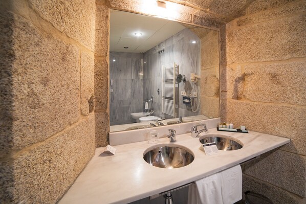 Un baño con pared de piedra, dos lavamanos, un espejo y una toalla colgada en la pared.