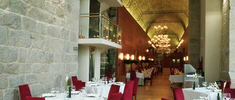 A restaurant with multiple dining tables, red chairs, and a stone wall.