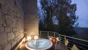 Un bain à remous sur une terrasse en bois, avec des murs en pierre, entouré de meubles d’extérieur et de bougies.