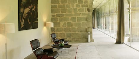 A lobby with stone walls, a large painting, leather chairs, a glass table, and a lamp.