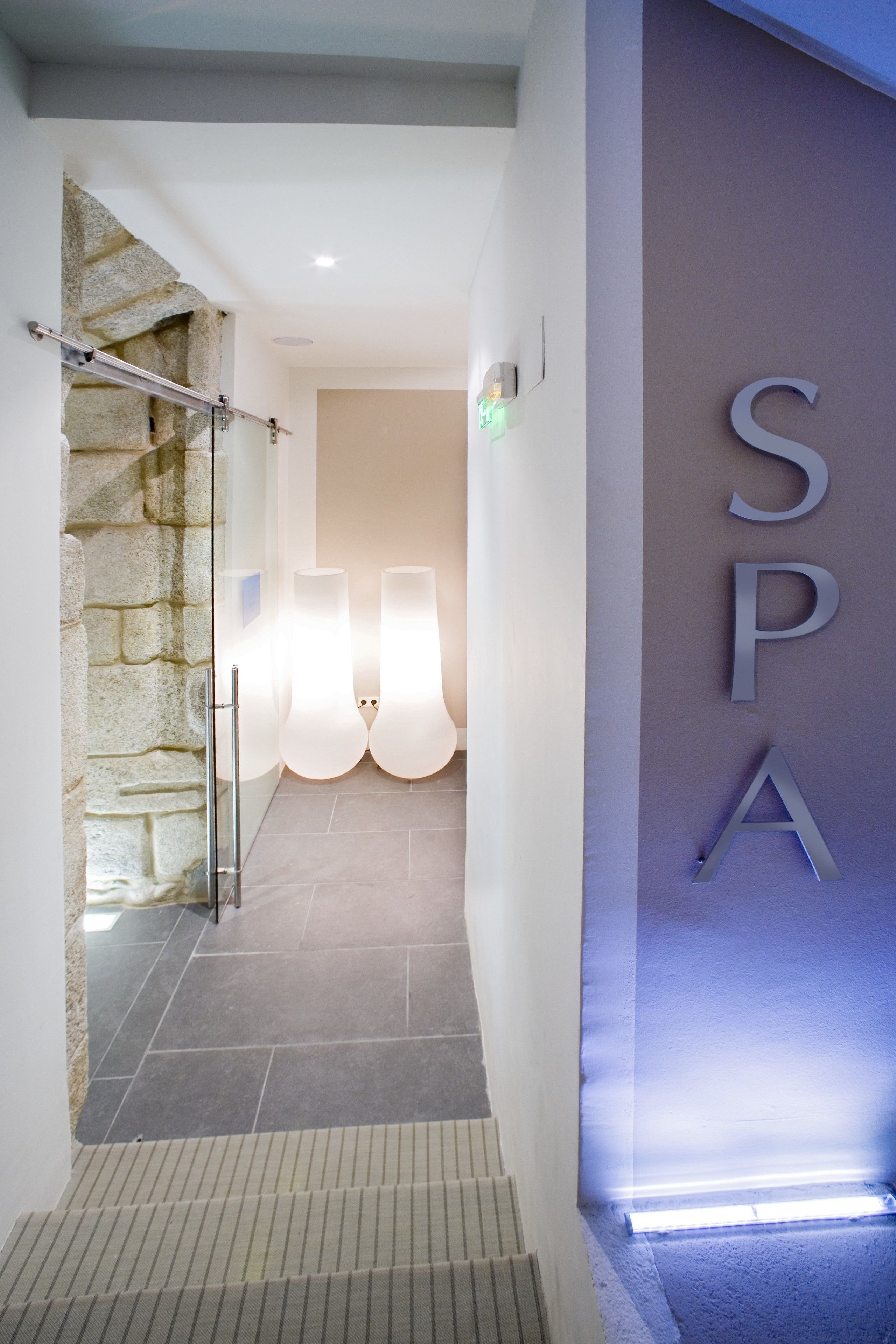 Entrada de un spa con pared de piedra, puerta de cristal y un letrero que dice 