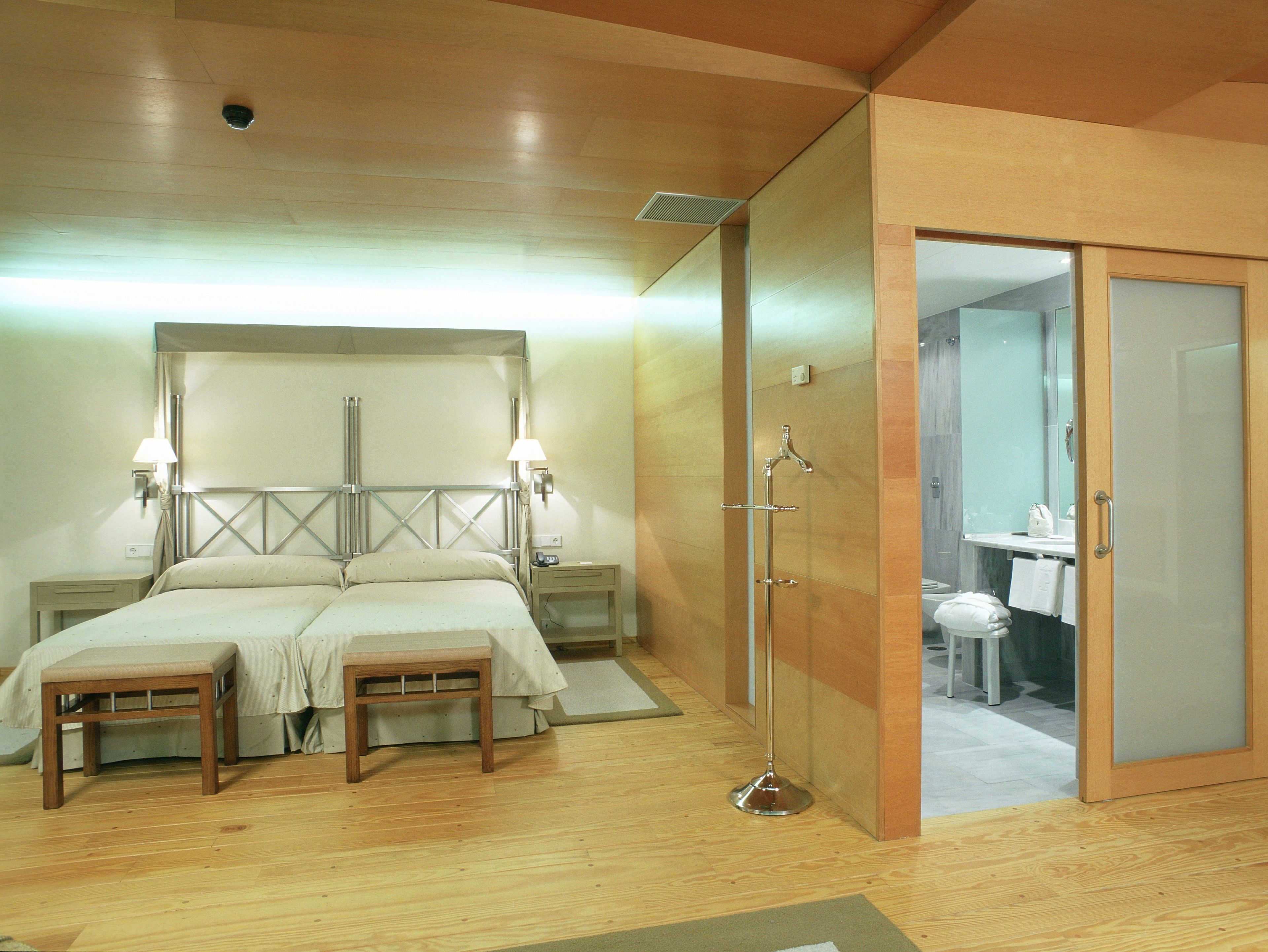 Habitación de hotel con piso de madera, una cama doble con dos mesitas de noche y un espejo.