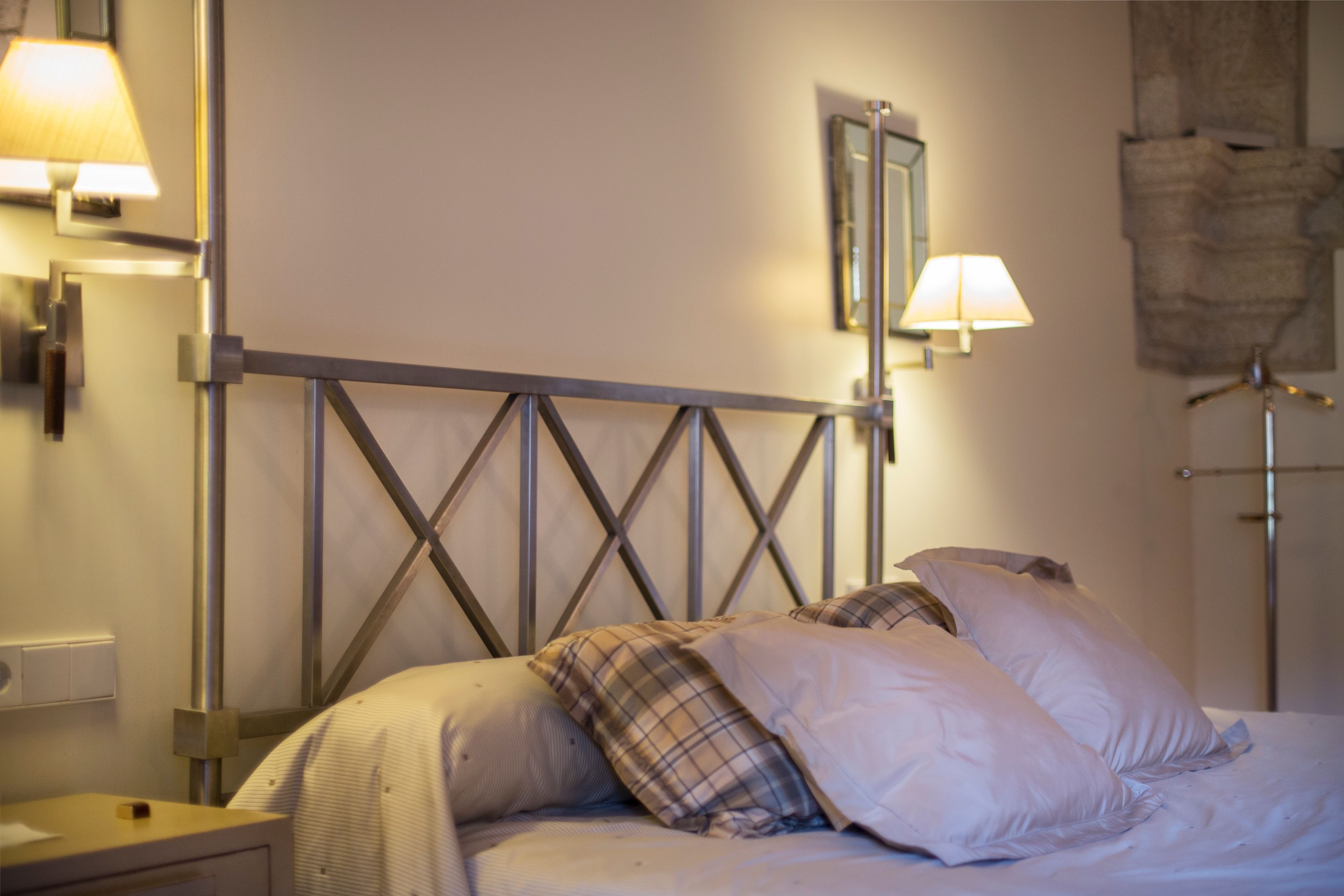 A neatly made bed with a metal headboard, two bedside lamps, and a wall-mounted mirror.
