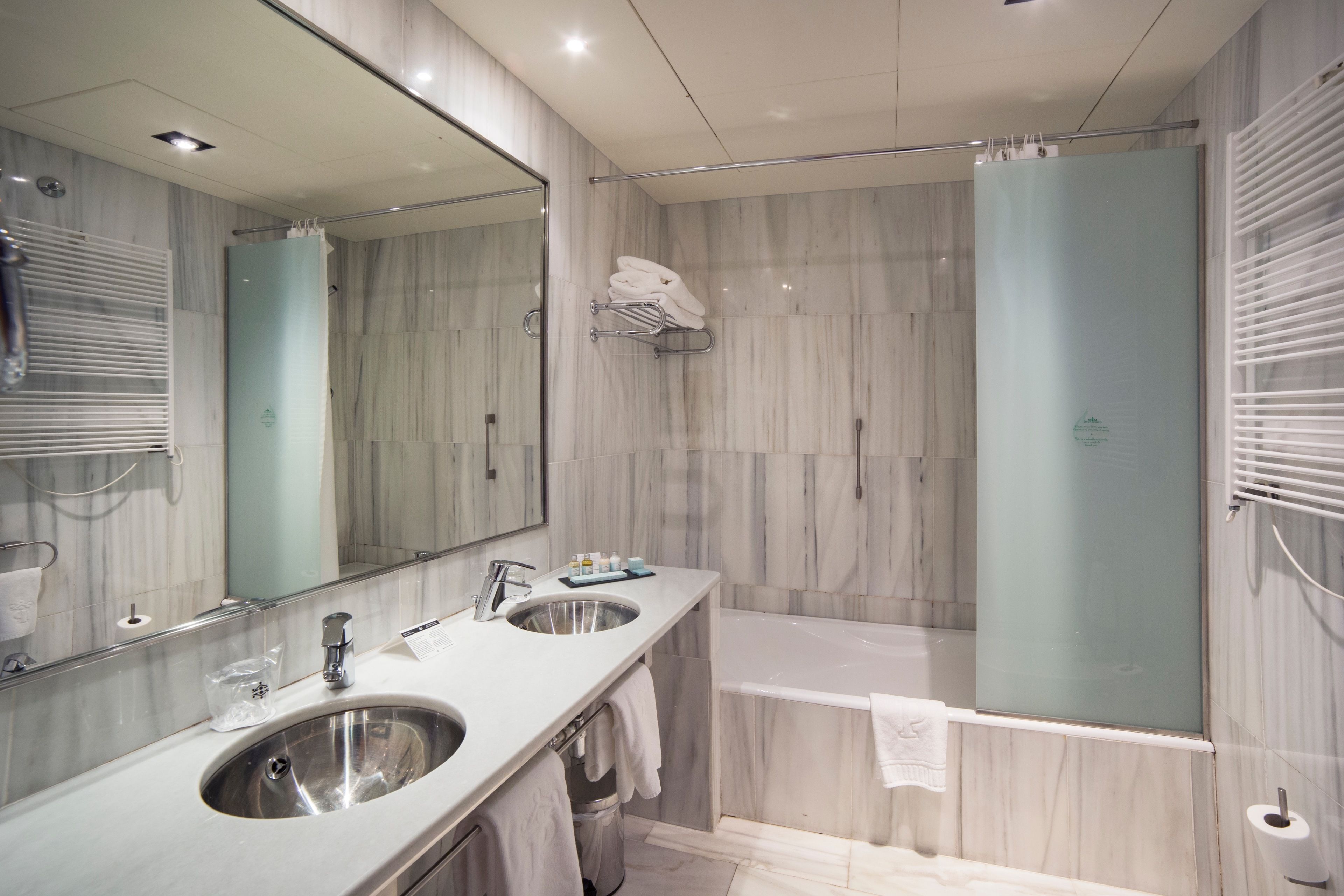 A modern bathroom with two sinks, a large mirror, a glass shower enclosure, and a bathtub.