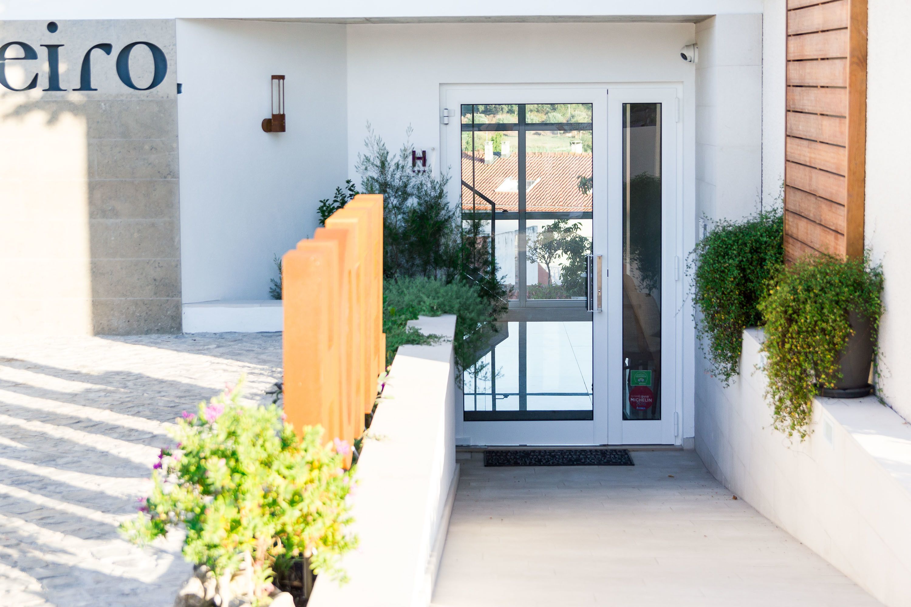 A modern building entrance with a glass door, a wooden bench, and potted plants.
