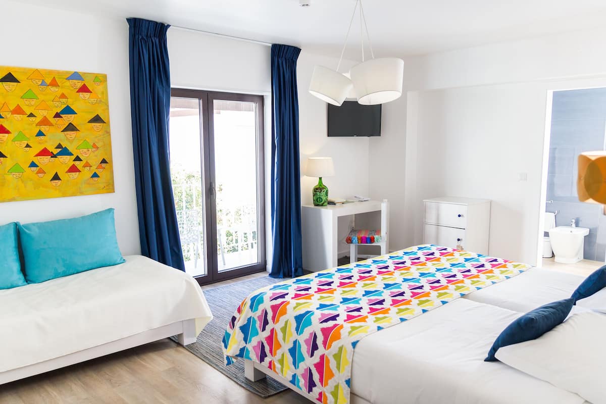 A hotel room with two beds, a desk, a chair, a TV, and a balcony.