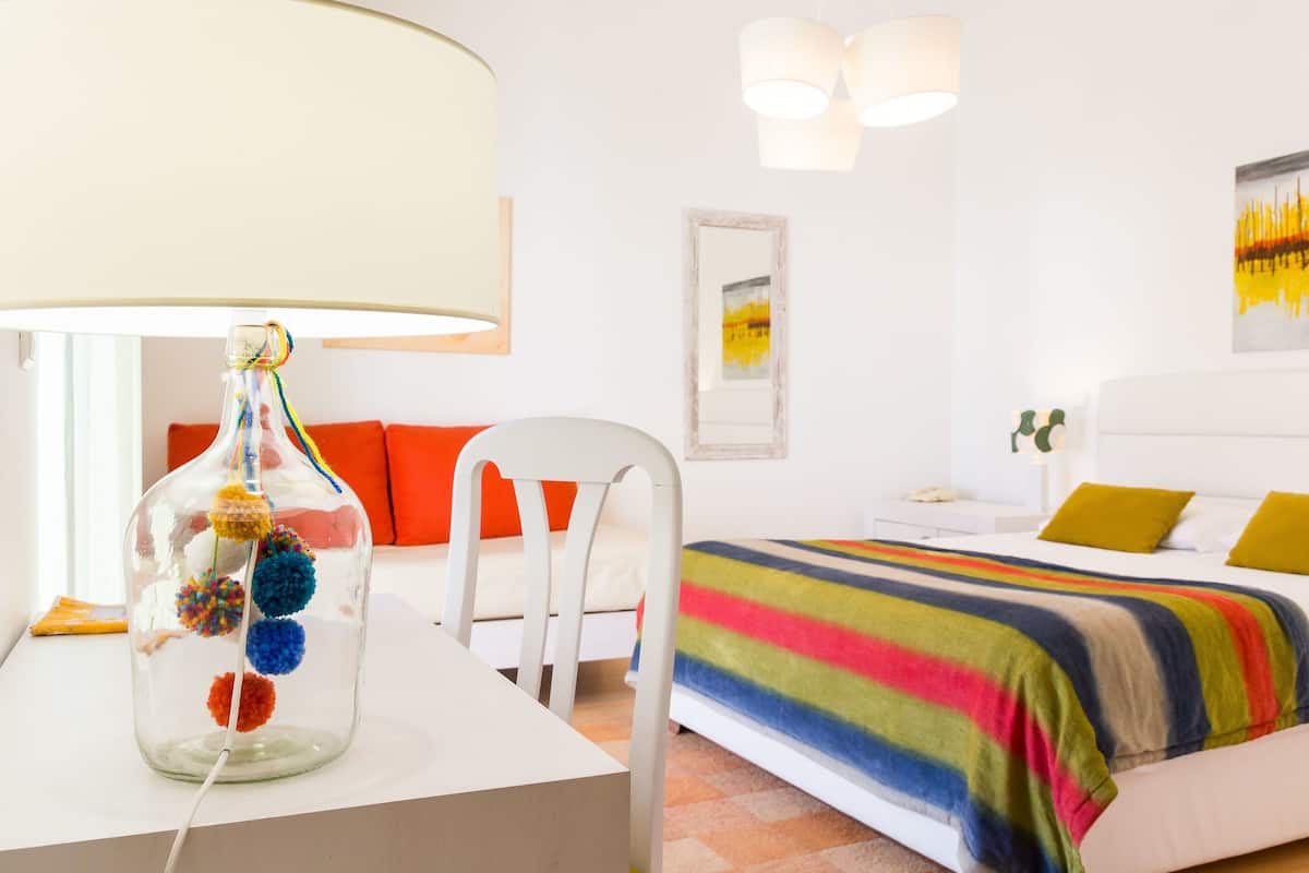 A hotel room with a bed, a chair, a lamp, and a decorative glass bottle.