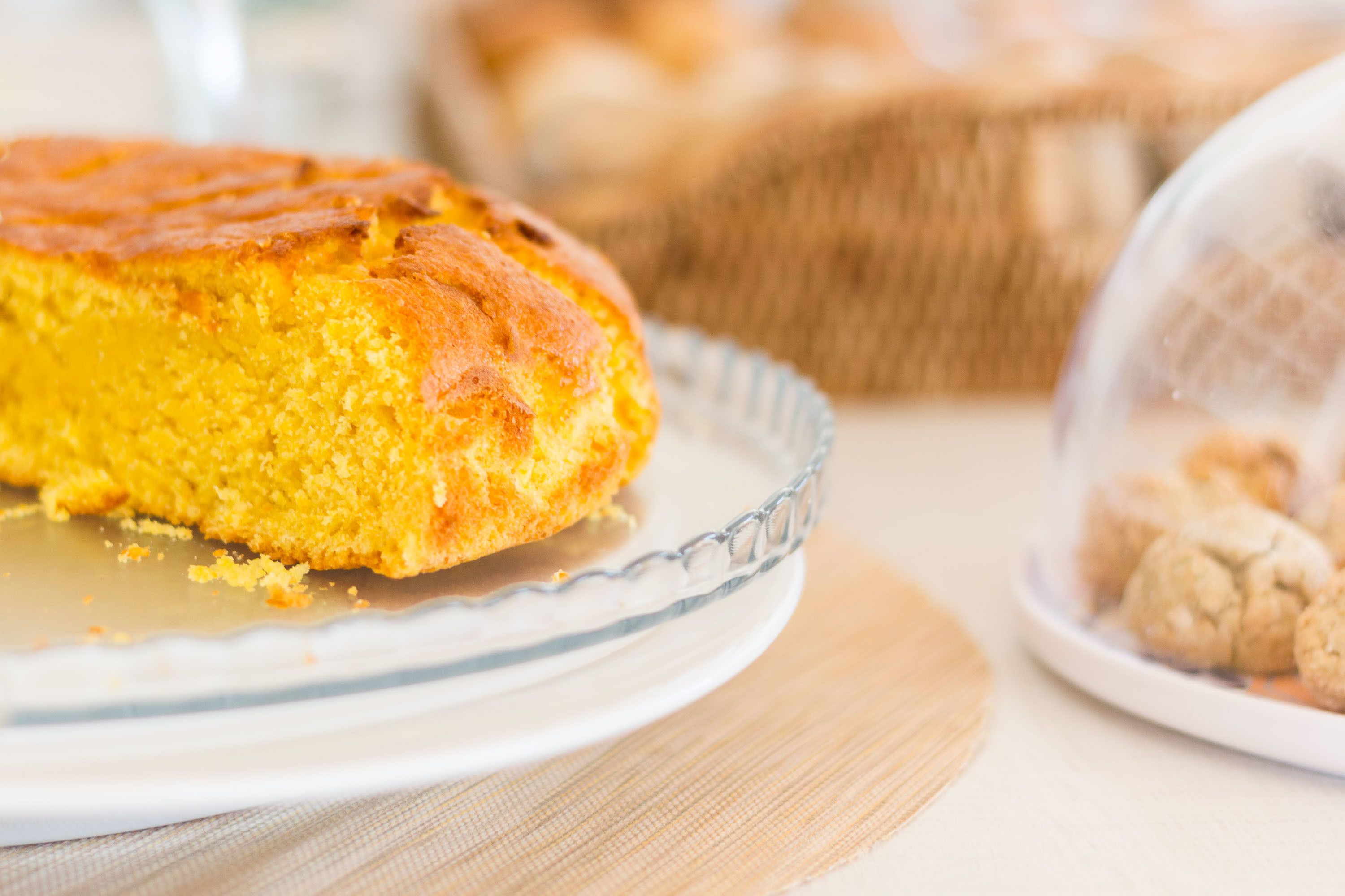 A round cake on a glass plate with a textured edge, placed on a table with a woven basket in the background.